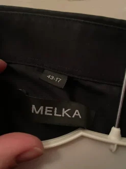 Musta kauluspaita rintataskulla